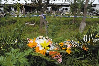 昨日，吉林省德惠市吉林寶源豐禽業(yè)有限公司燃燒事故現(xiàn)場警戒線外，遇難者家屬在路邊擺放了花圈祭奠逝去的親人。吳江 攝