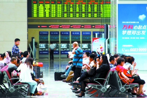 候車(chē)大廳溫度很高，一名乘客一手扇風(fēng)、一手擦汗