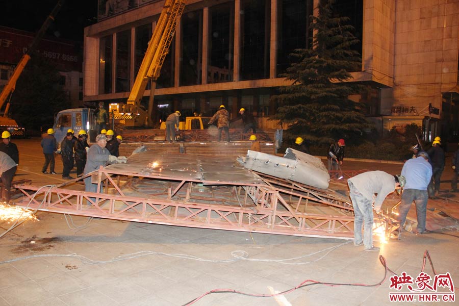 地面上的20多名工人對吊裝下的廣告牌進行分割。