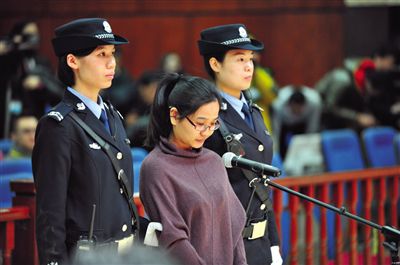 被告人盧梅低著頭，站在朝陽法院刑事審判庭的被告席上。